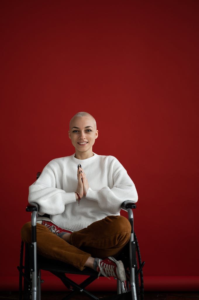 Young smiling female sitting in Lotus pose while looking at camera during cancer rehabilitation process on red background